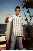 Young man holds up a nice steelhead while standing on boat.